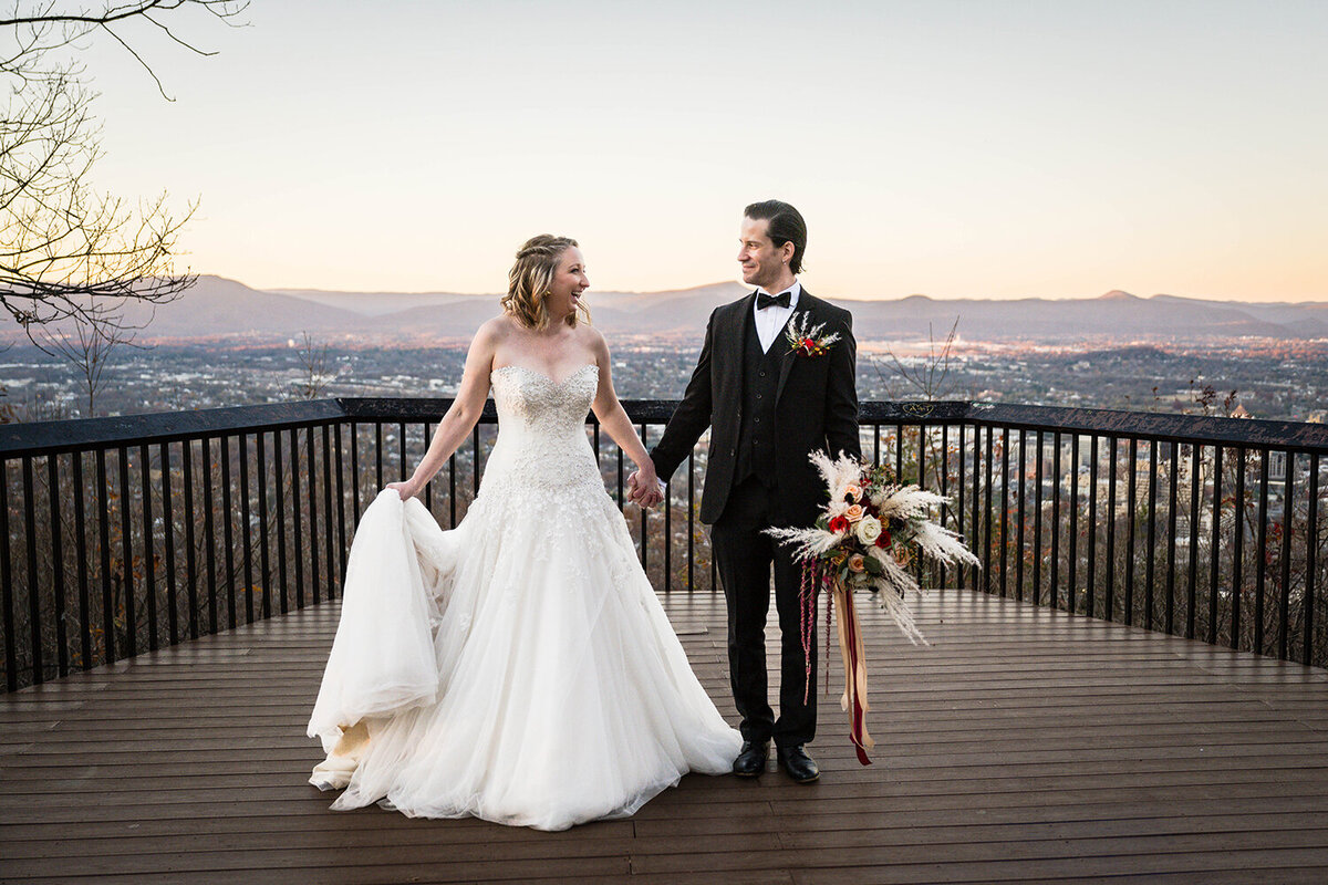 A bride and groom hold hands at Mill Mountain’s Rockledge Overlook at sunset during their elopement in Roanoke, Virginia.