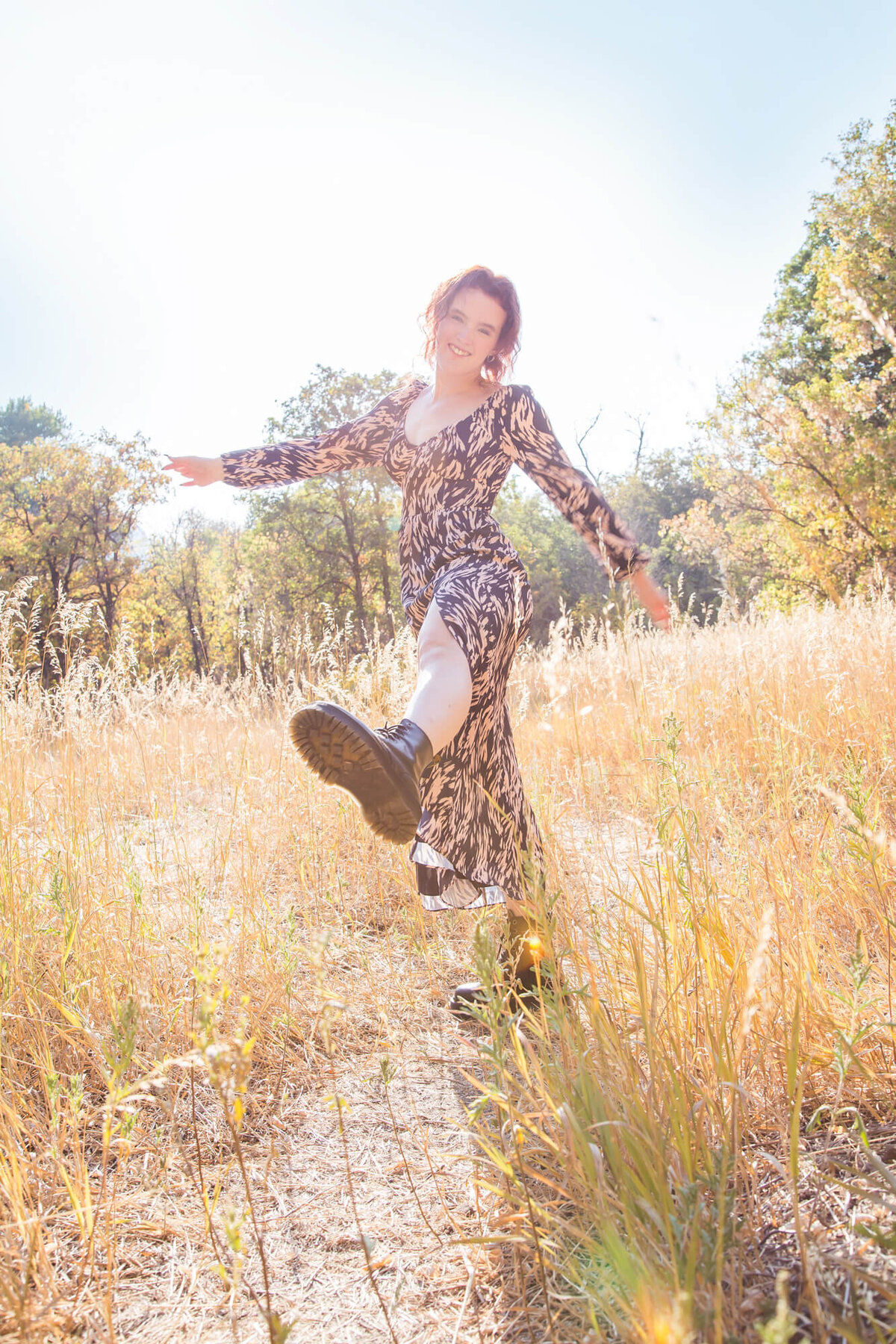 redheaded young woman danicng in a mountain field for her senior portrait session with las vegas milestone photographer