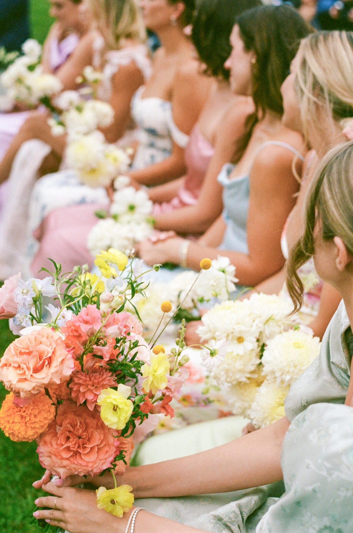 Grainy colour photo shot on 35mm of bright bridesmaids bouquets and brightly coloured bridesmaids dresses at an outdoor wedding in Prince Edward County