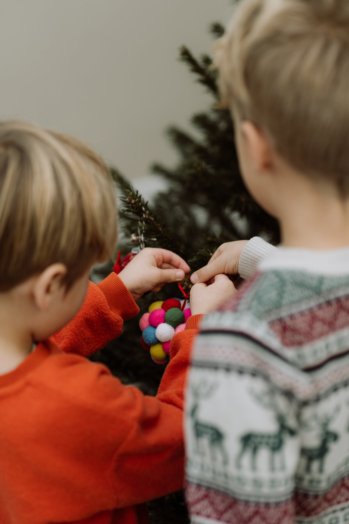 Lifestyle fotoshoot van een gezin dat samen de kerstboom optuigt, met focus op de gezelligheid en de kleine, magische momenten van de feestdagen.