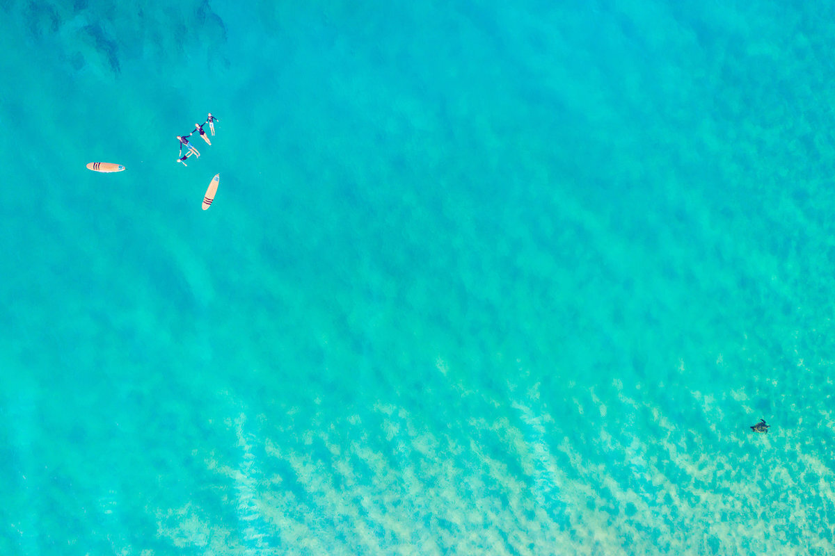 Family on surfboards floating the ocean off Wailea on the island of Maui photographed by Love + Water using drone
