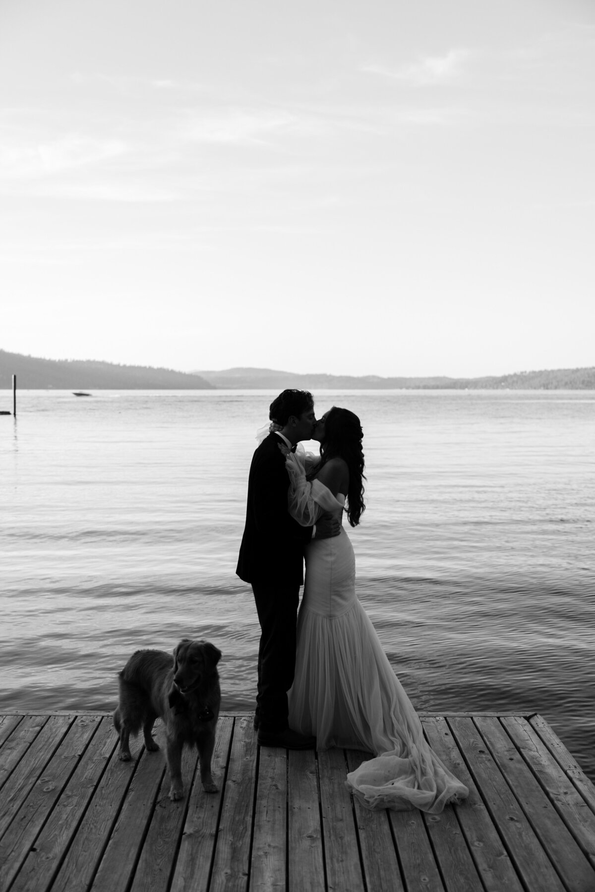 Bride and groom kissing on a dock with a dog