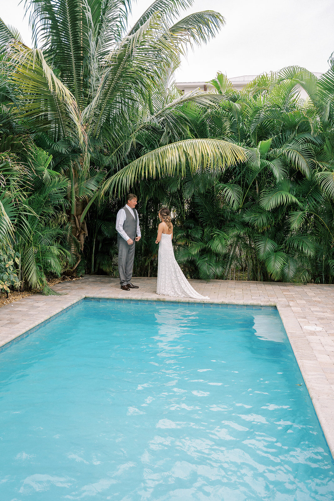 bride and groom standing under palm trees near a pool