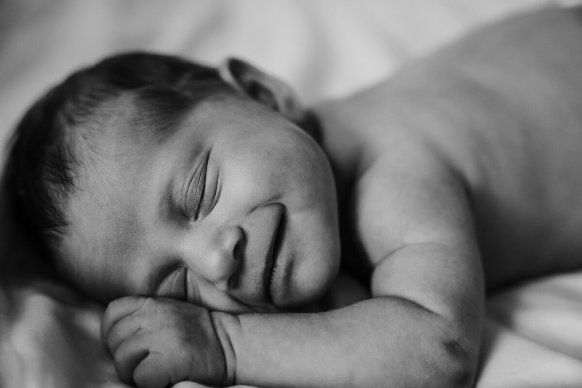 Newborn Photographer, a baby boy seemingly smiles as he lays asleep in crib