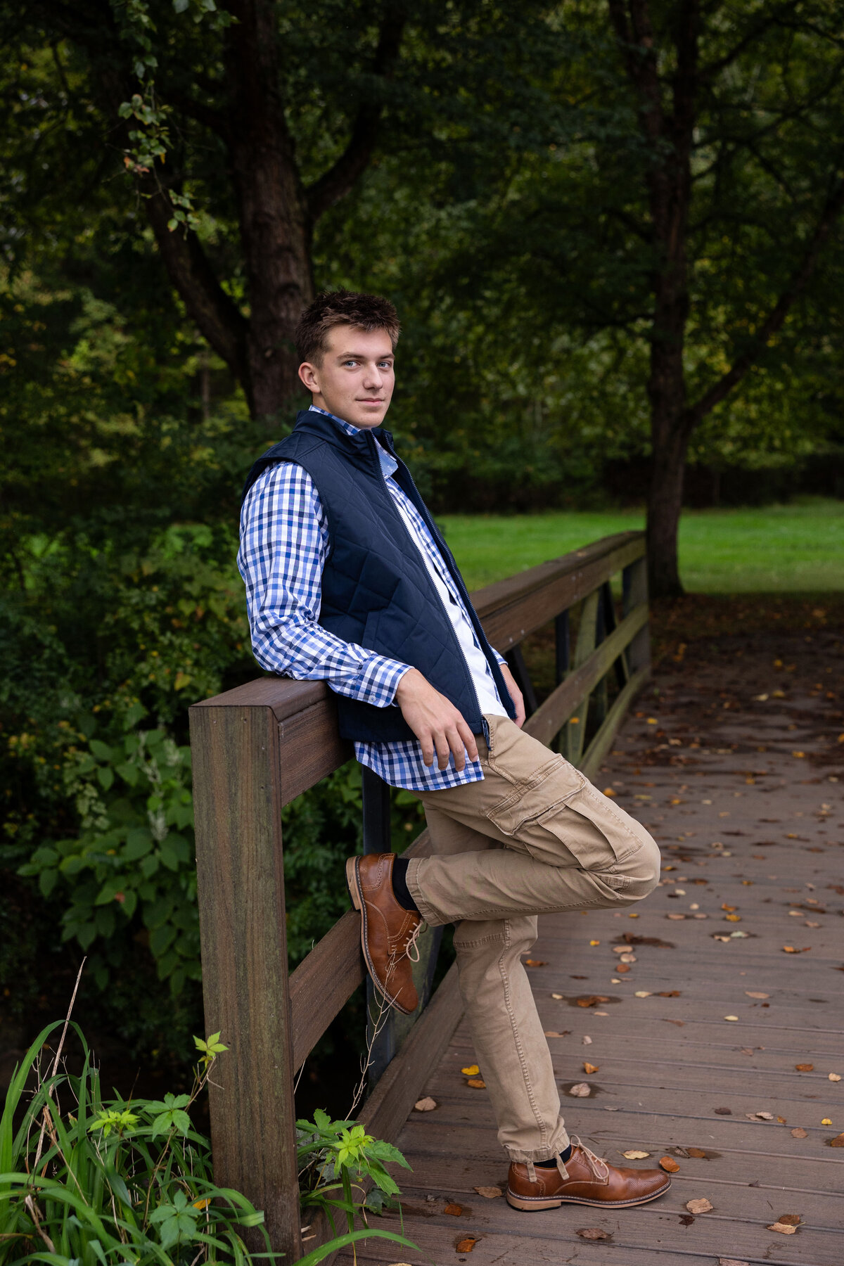 boy poses next to bridge railing as he looks without smiling for his portraits with fall leaves in Latrobe pa.