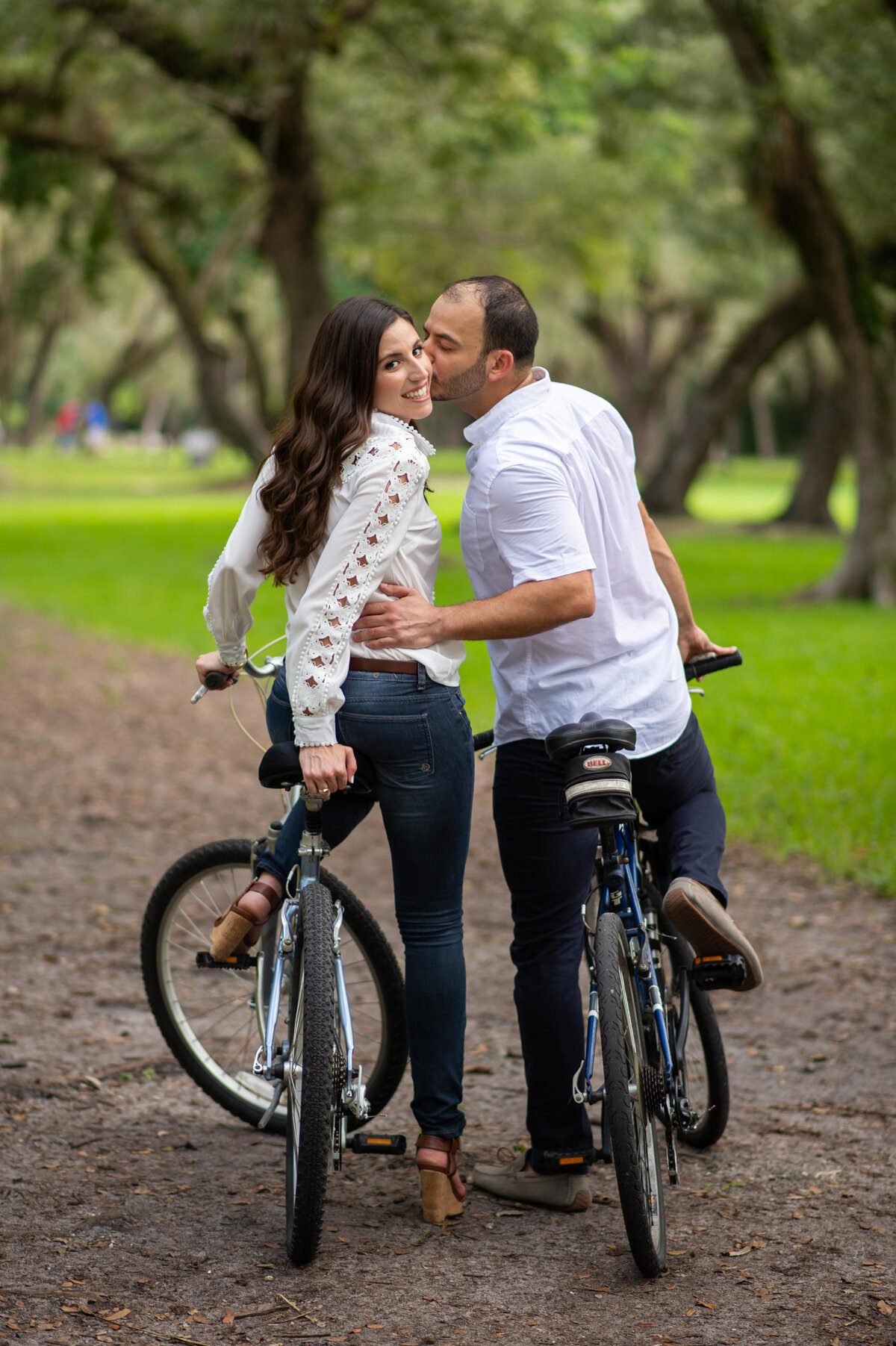 Couple sharing a sweet kiss while riding bicycles in a lush, green park."