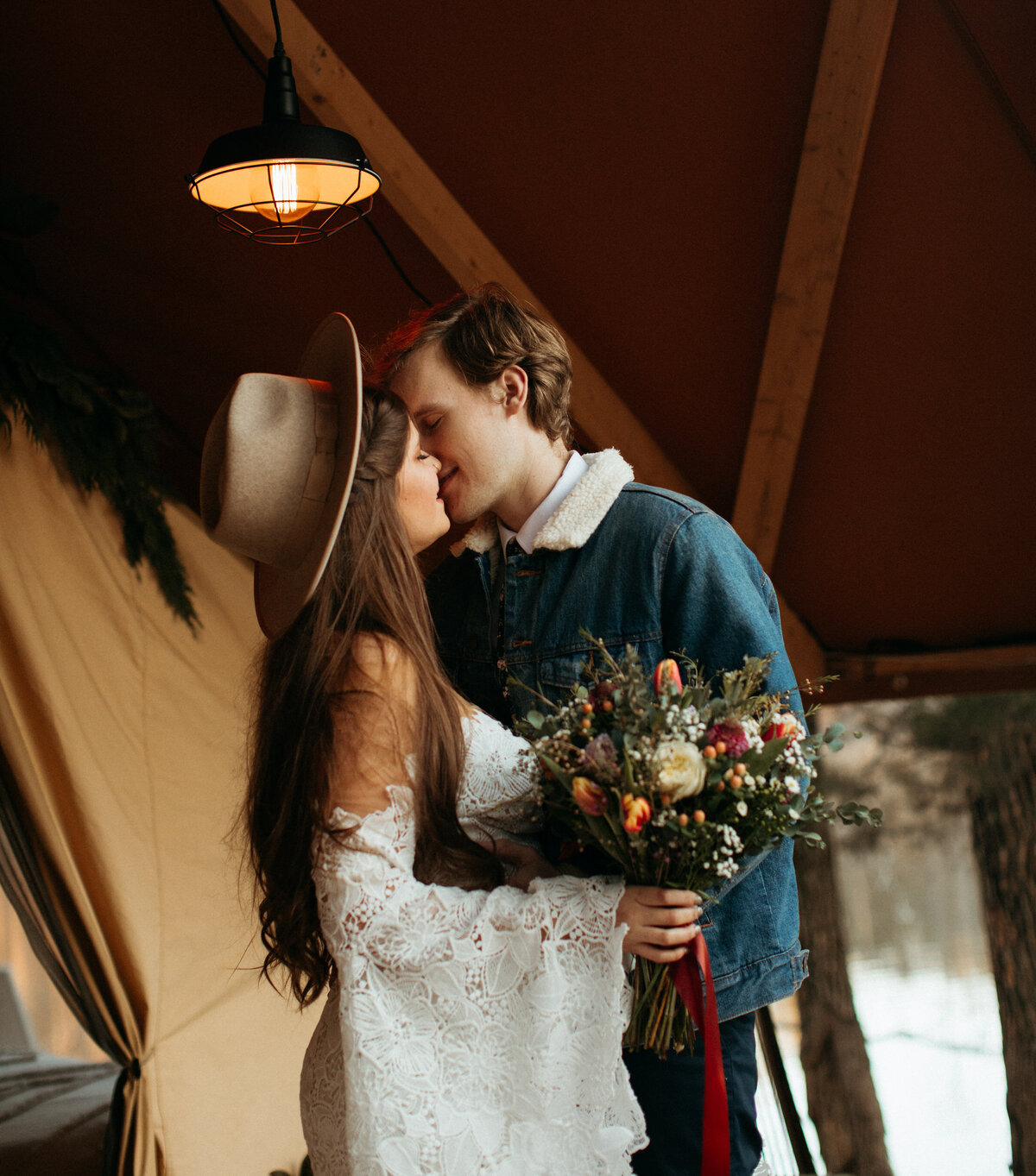Groom kissing his boho bride on the porch of their lakeside tent the morning of their elopement