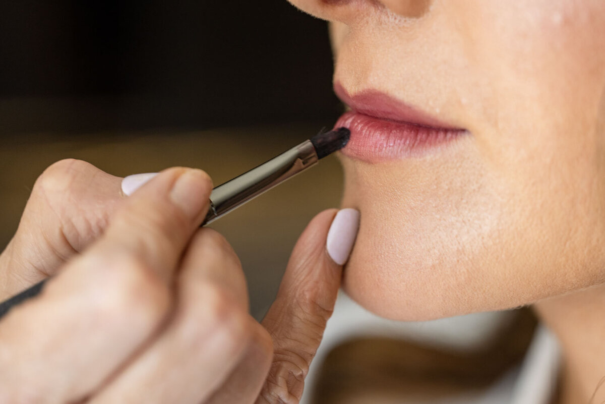 A woman is applying lipstick to her lips with a brush