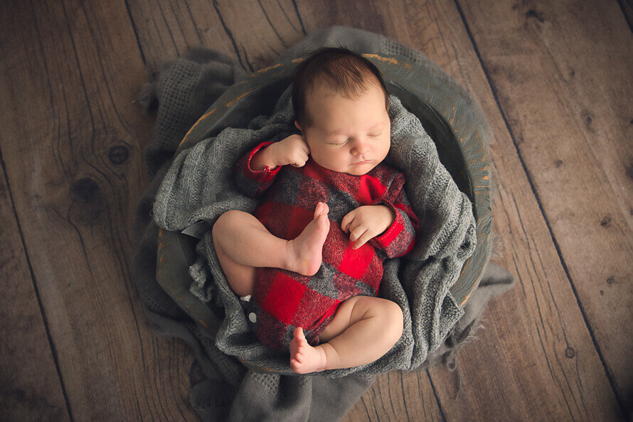 Newborn baby in Christmas outfit sleeps in a gray bowl.
