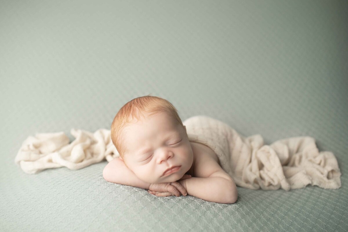 Red-headed newborn boy peacefully resting on his back, hands gently placed on his chest, on a dreamy fabric backdrop