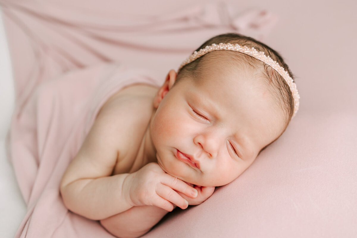newborn baby girl sleeping on pink blanket with her hands under her chin