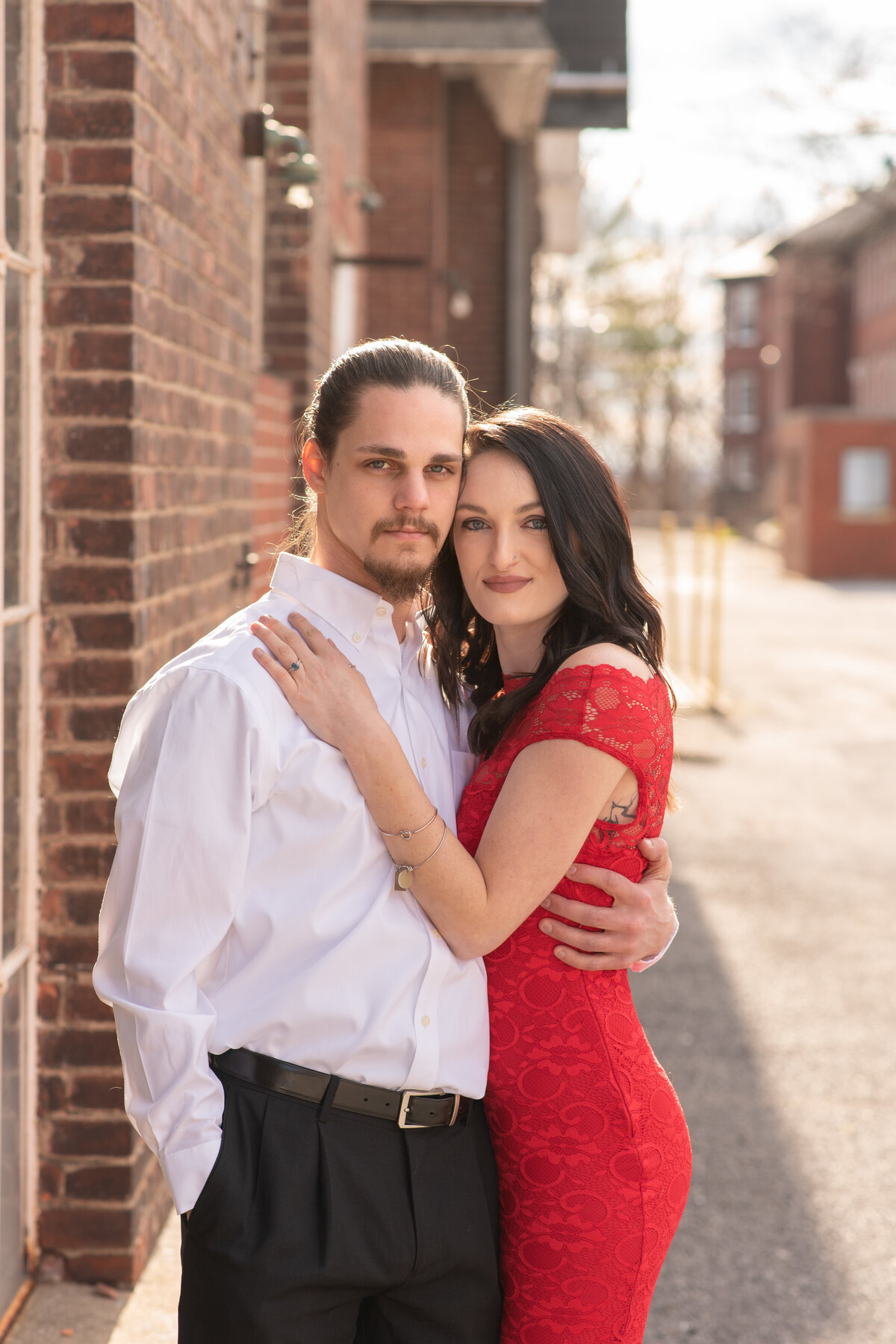 Engaged couple in dressy attire with brick buildings around them
