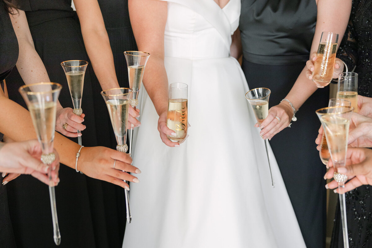 close up of stemmed champagne glasses held by the bride and bridesmaids at The Adolphus in Dallas, highlighting elegant drink presentation during the wedding celebration.
