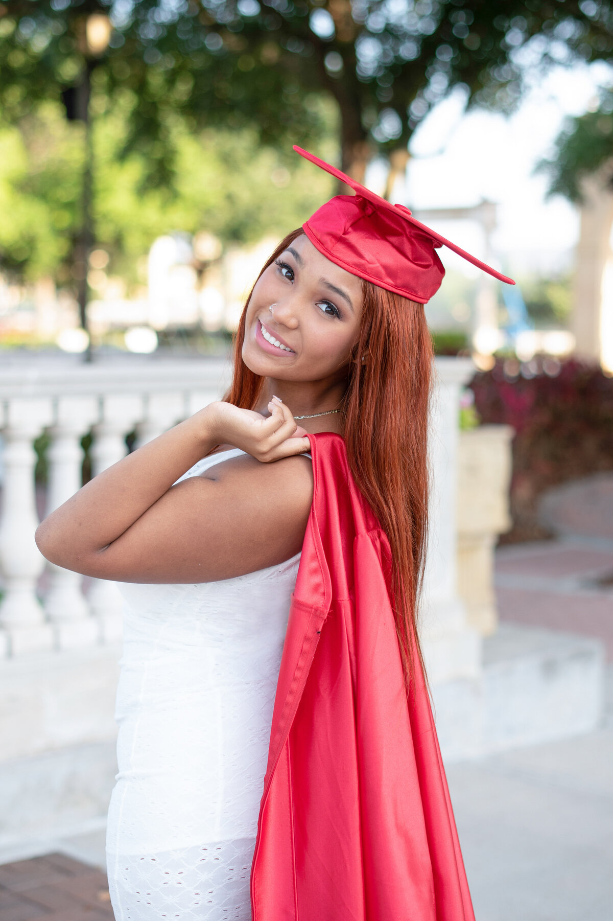 High school senior girl wearing cap and holding gown over her shoulder.