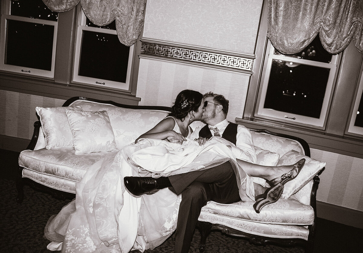 high flash editorial black and white photo of bride and groom sitting on couch with sunglasses