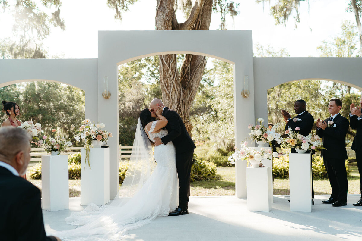 Bride and groom share their first kiss under the ceremony arch at Uliana Estate in Lakeland FL.

