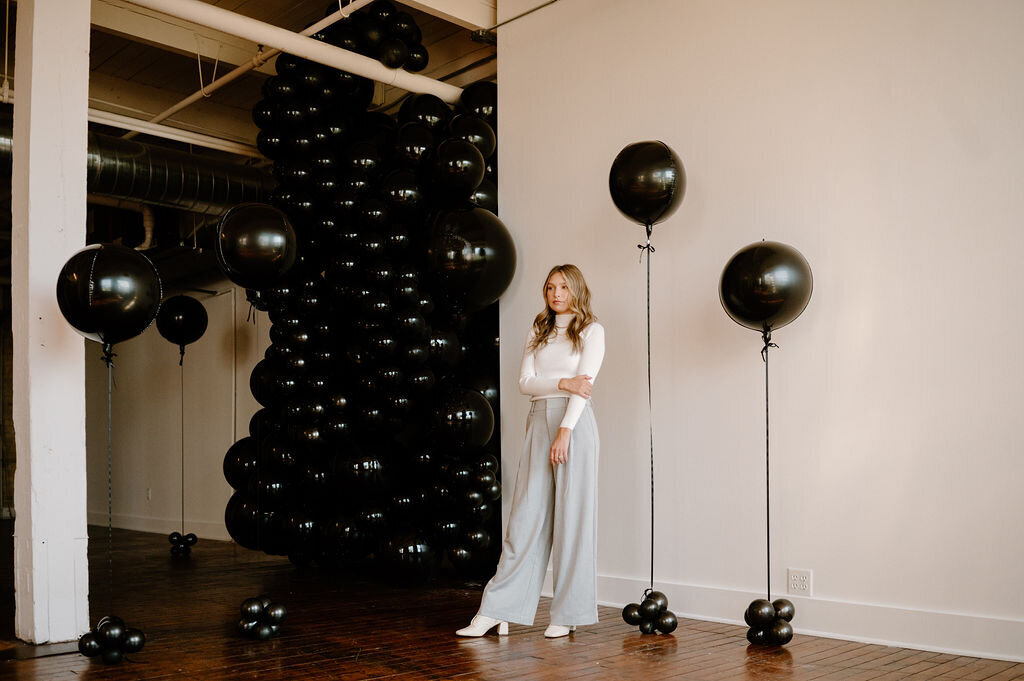 Sandra standing with dramatic black balloon installation for a chic event photoshoot