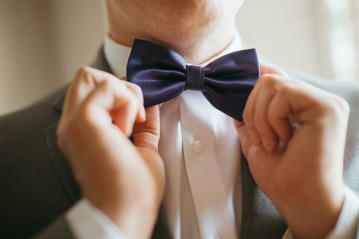 a groom getting ready and fixing his bow tie