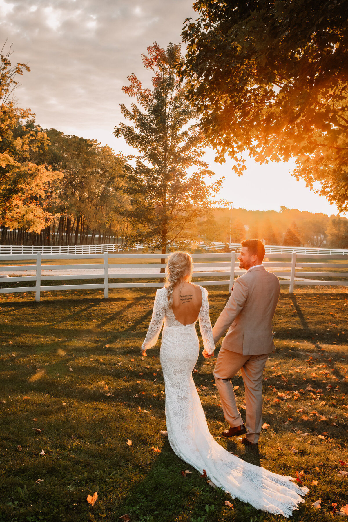 bride and groom hold hands while walking into the sunset in a field