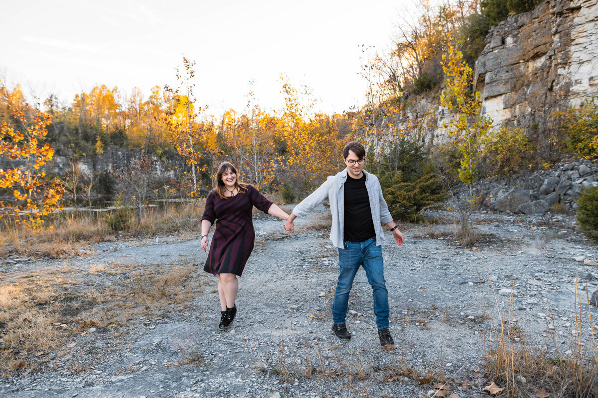 An engaged couple walks hand in hand through a quarry laughing
