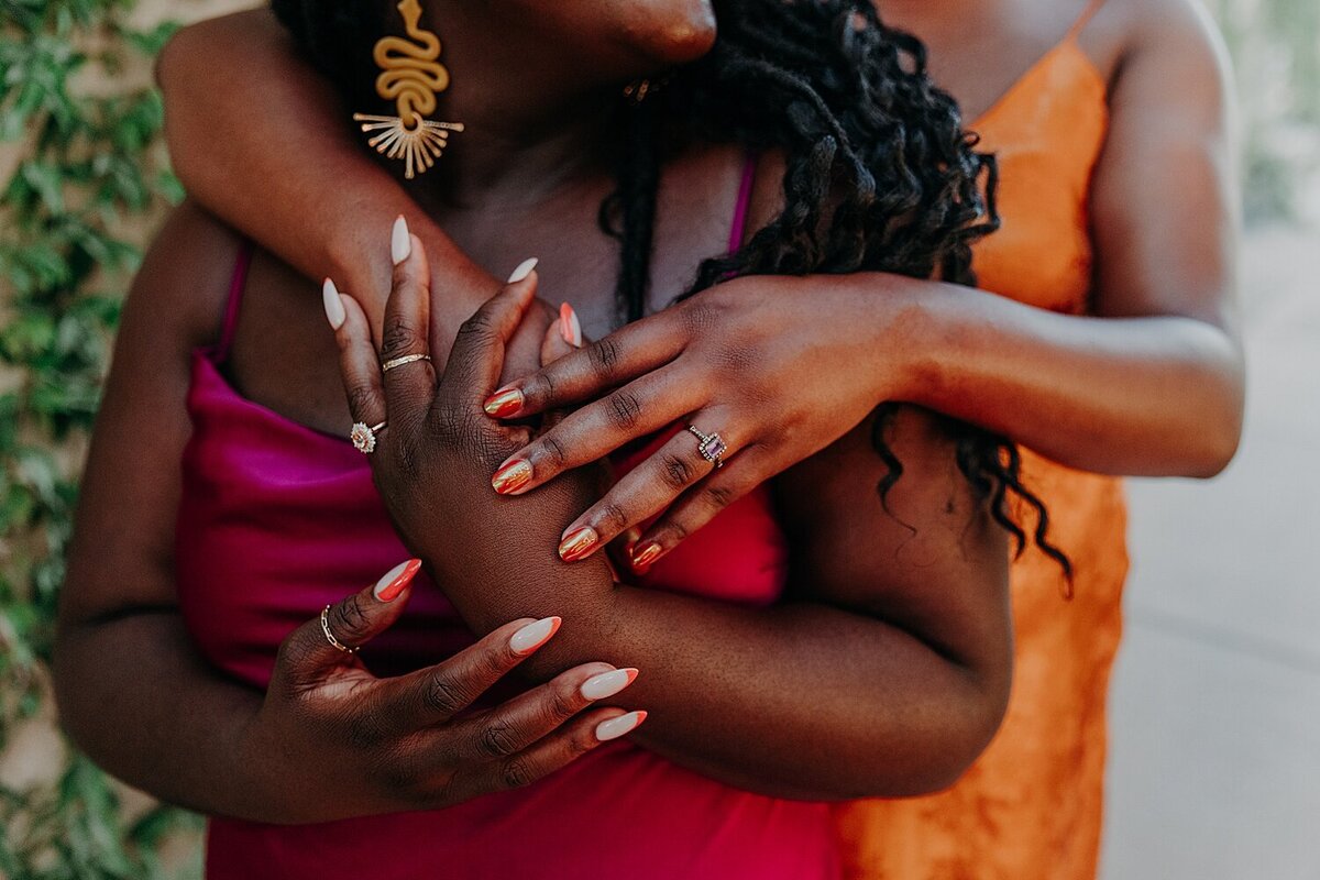 two women of color cuddle together and show engagement rings