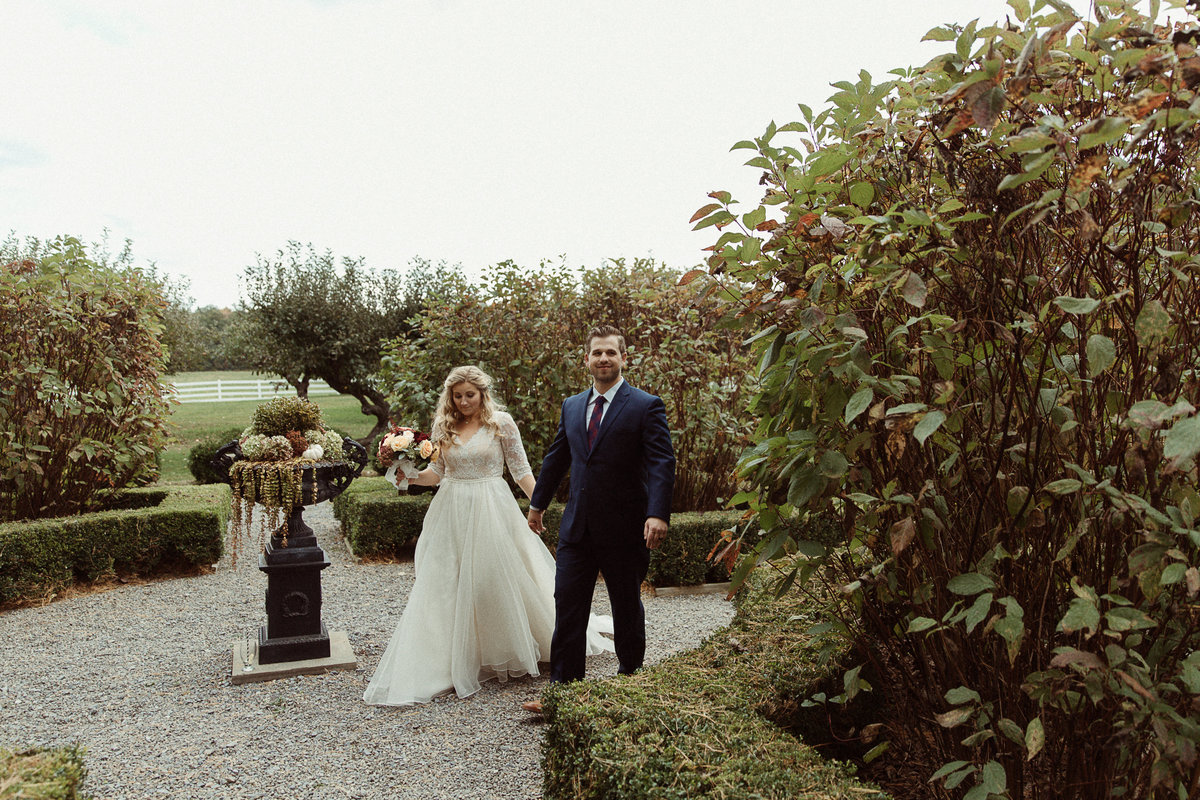 bride and groom hold hands and walk through lush gardens