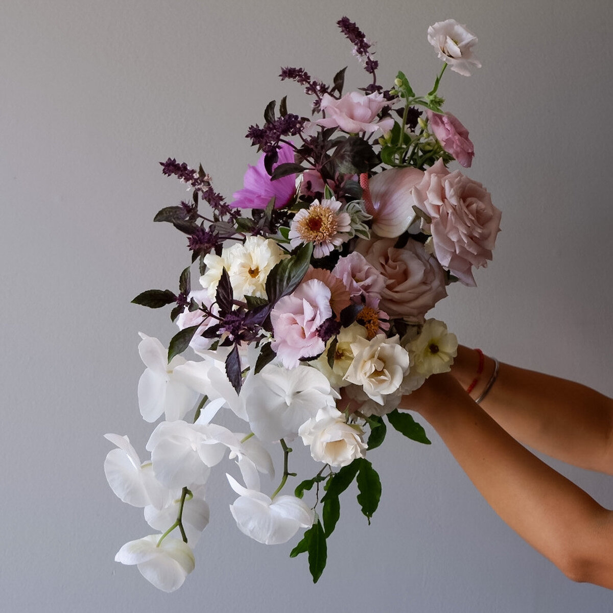 Close-up of a hand holding an elegant bouquet featuring white orchids, blush roses, and deep burgundy florals