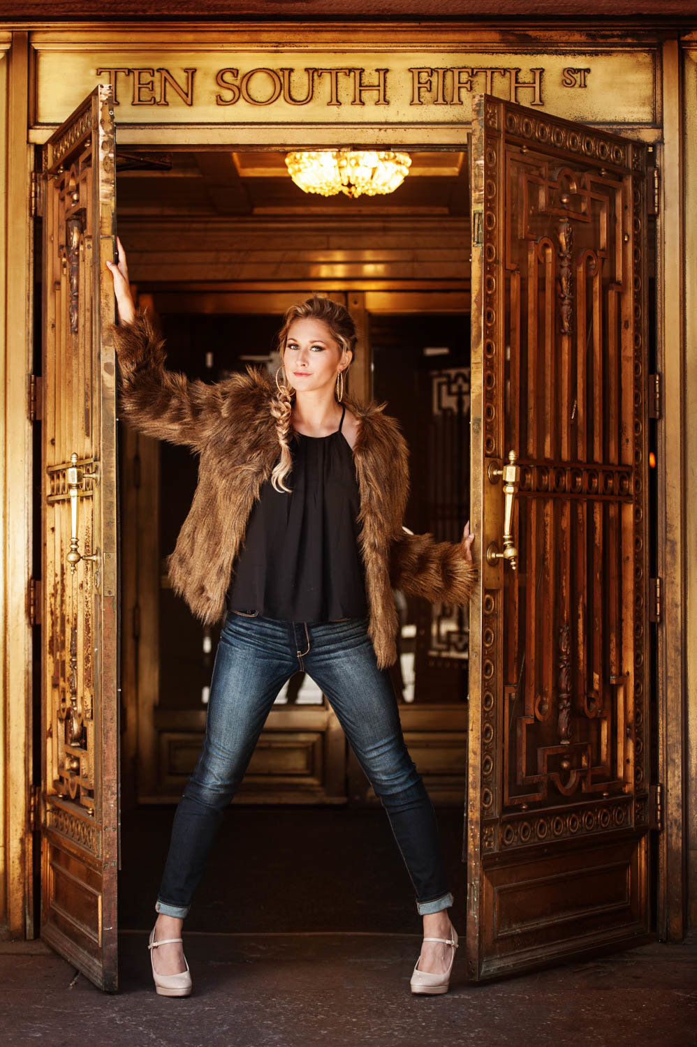 high school senior photo of fashion girl in fur jacket  leaning against a gold door