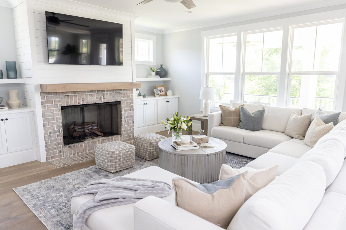 Bright coastal living room with neutral sectional, textured ottomans, and brick fireplace styled with layered décor by KASL Design Co.