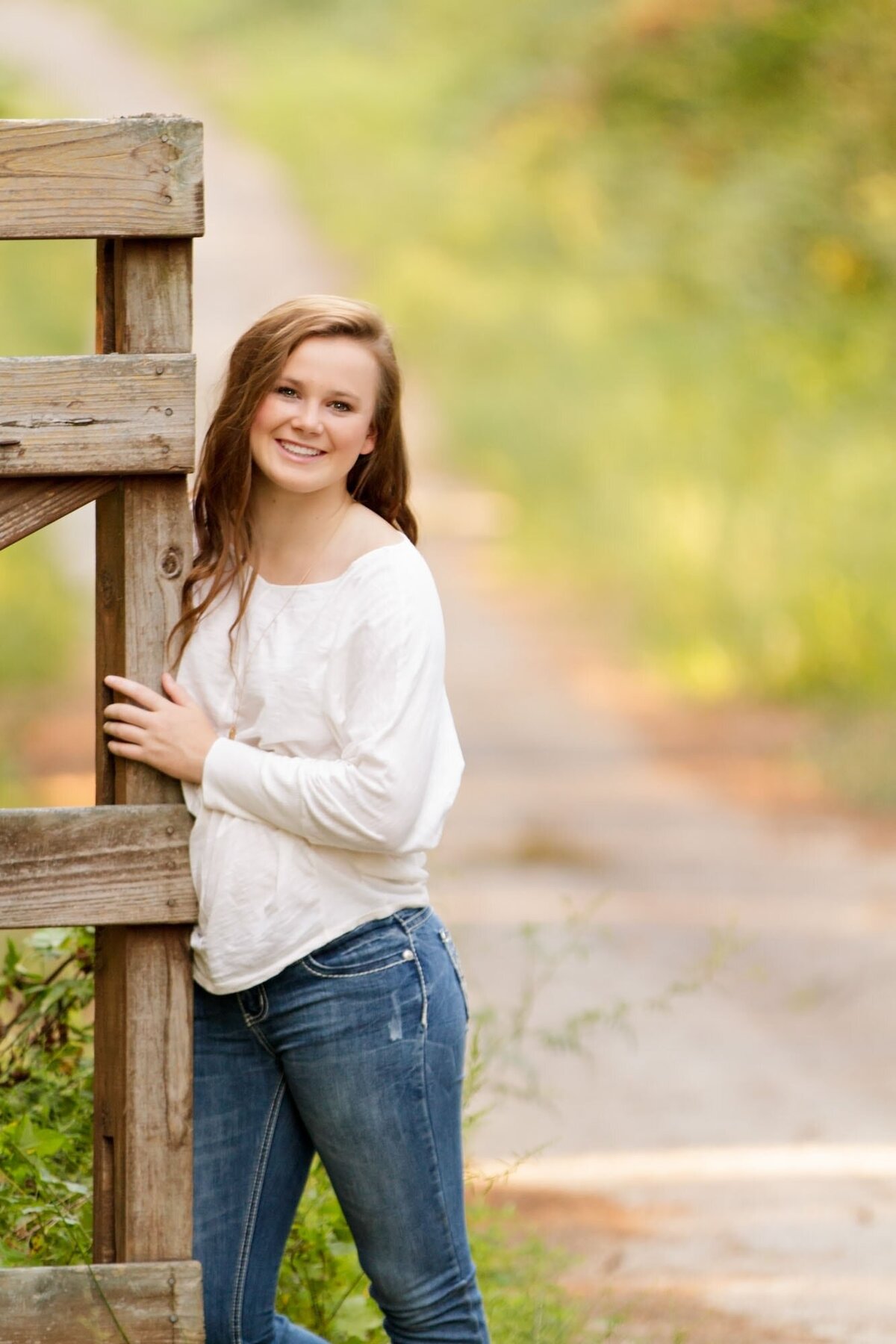 Senior portrait of a girl leaning against a fence post.