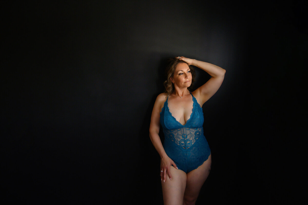 woman wearing a blue lingerie with her hand in her hair against a black background for her Toronto boudoir photos.