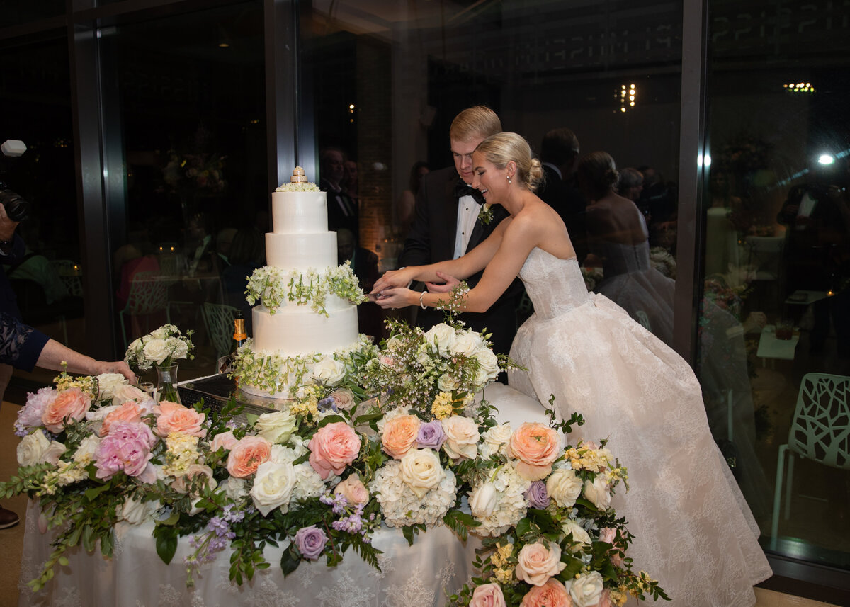 Bride and Groom cutting their wedding cake surrounded by peach florals in Jackson, Mississippi.