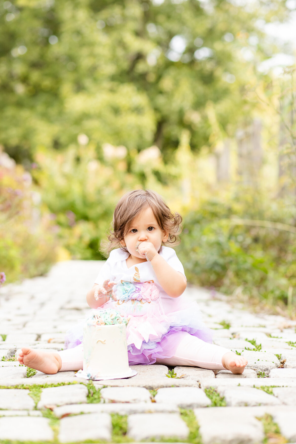 First birthday girl eating birthday cake looking intently at camera