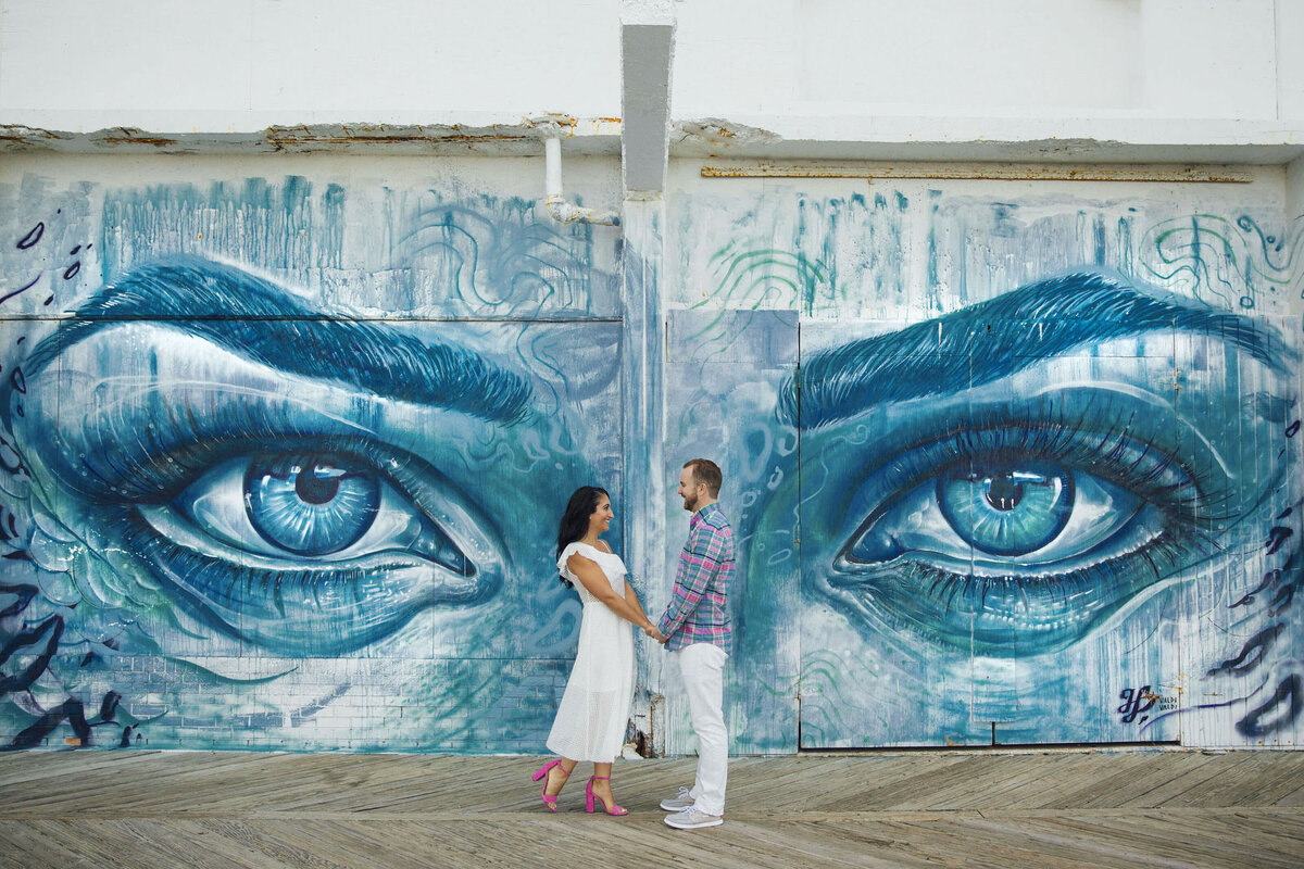 Smiling couple in front of Blue Eyes mural during engagement session in Asbury Park New Jersey