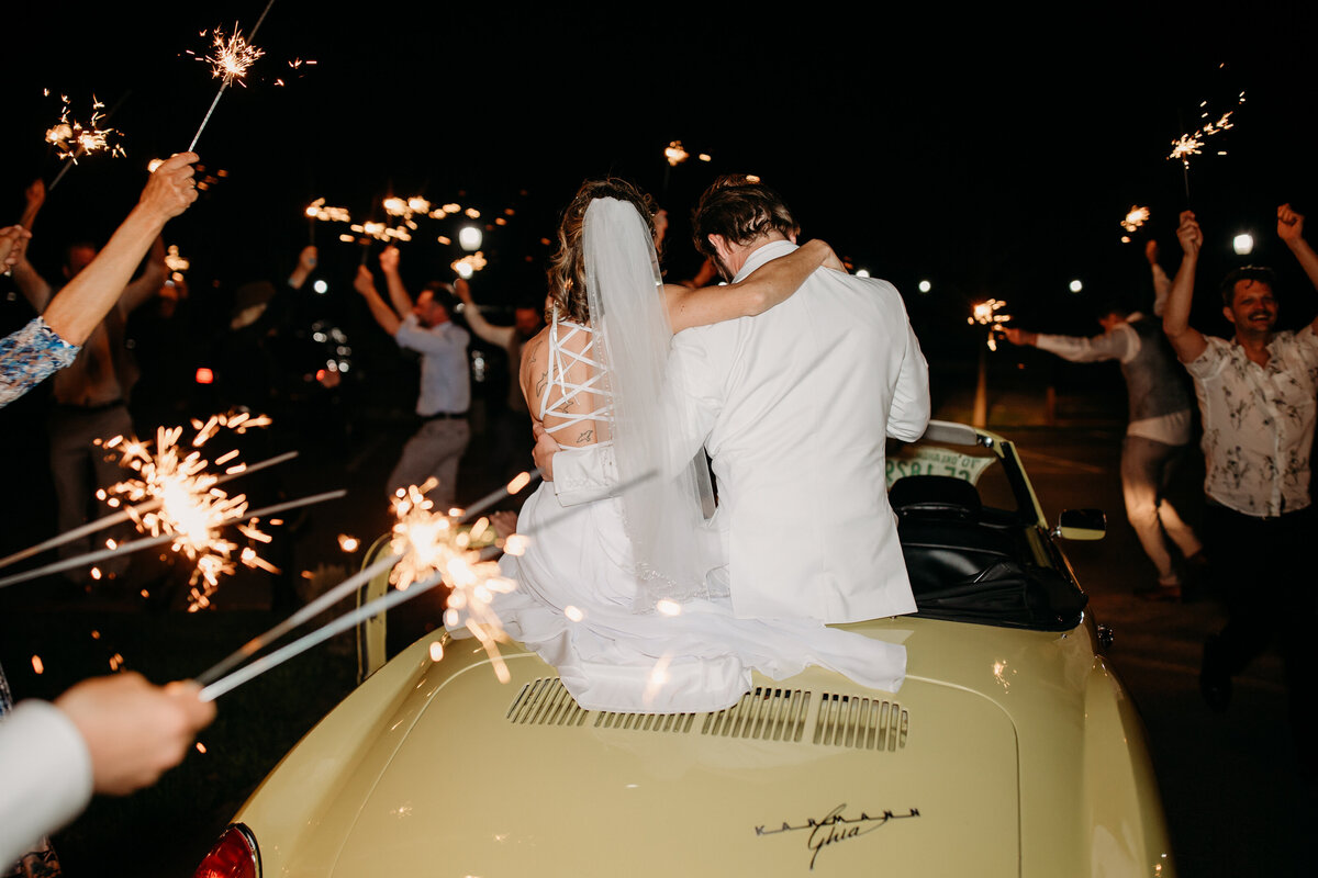 Bride and groom making an exit in a vintage convertible as guests wave sparklers