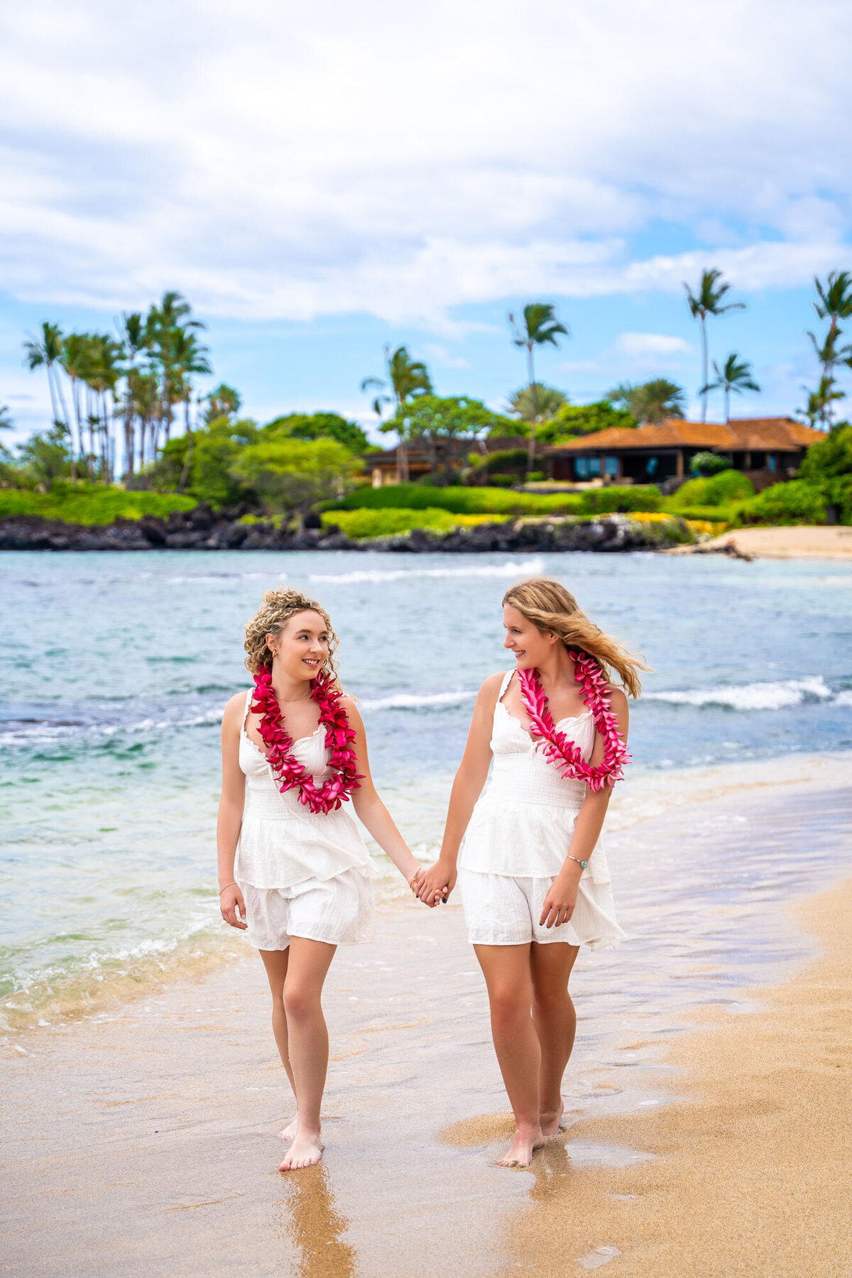 Two girls holding hands and looking at each other on Kukio Beach, by Hawaii family photographer