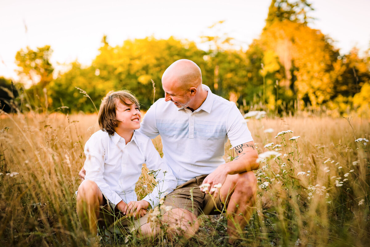 Father and son enjoying quality bonding time during their family photoshoot at Discovery Park, Seattle WA. Photograph is infused with Maë Lans Photography's signature, glowy hues amidst the tall yellow grass and golden light.