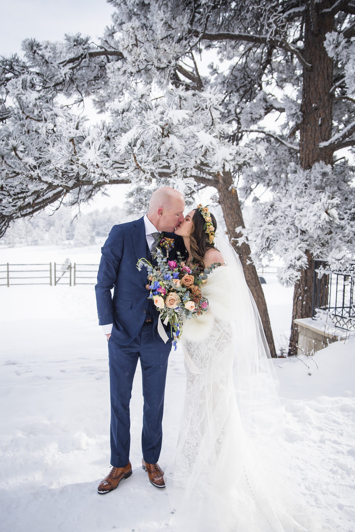 A bride and groom share a kiss in the snow.