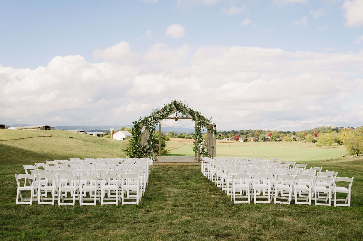 Sunny Slope Farm outdoor ceremony space with a frame of a house decorated with floral arrangements with white foldable wood chairs facing the house frame with rolling hills in the distance for a Shenadoah National Park wedding