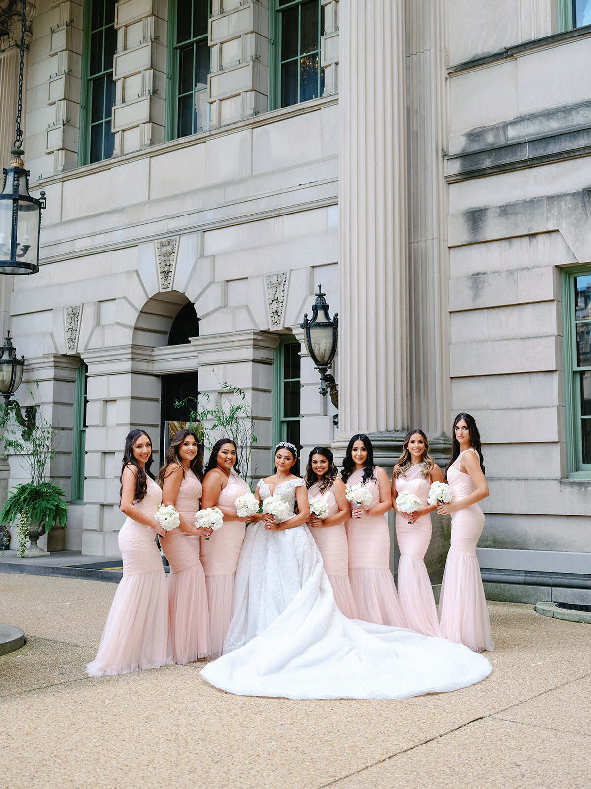 Bridal party wearing pink tones stands in front of Larz Anderson House