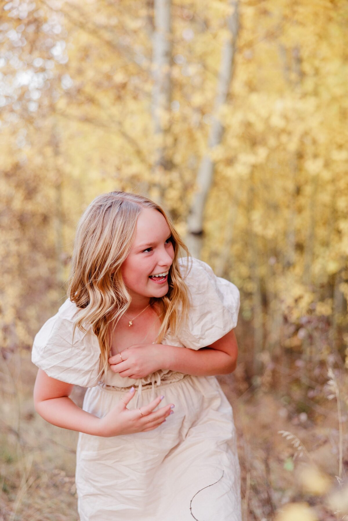 A teen girl laughs while on a hike through Aspens in fall
