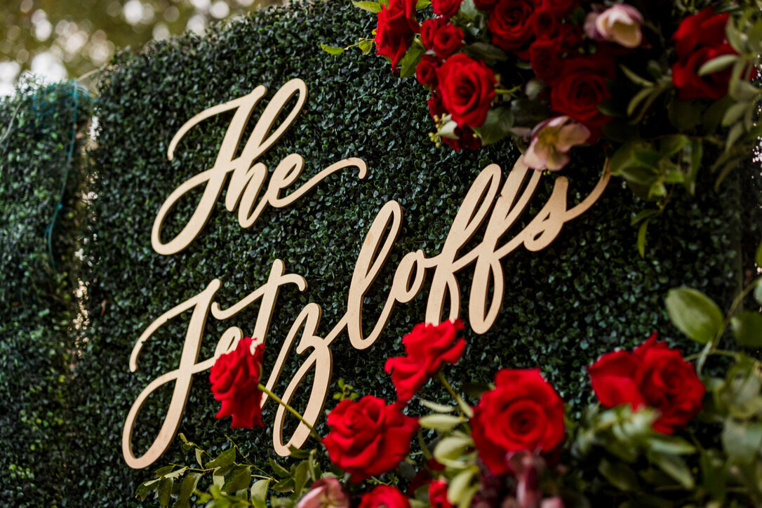 Last name signage, red flowers, tucked in flowers, red flowers, red roses, gold accents, hedge, grass wall 