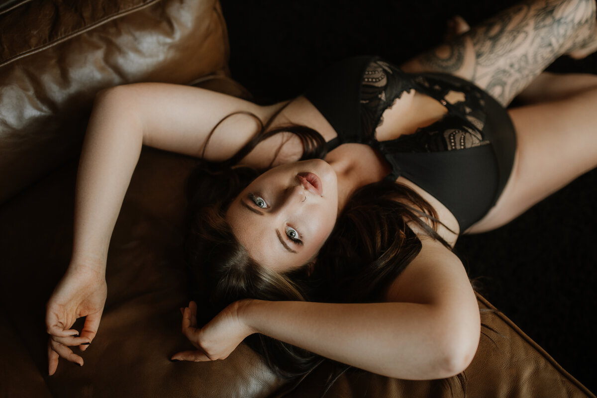 A woman in a black bodysuit poses on the couch during her boudoir session.