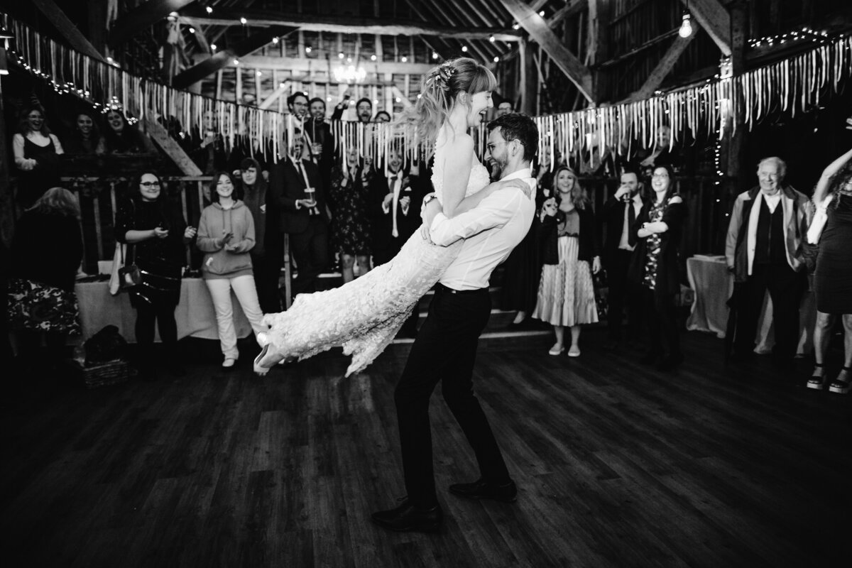 Black and white photo of groom picking up bride in joyful pose