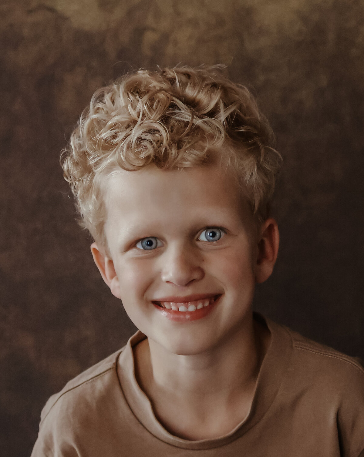 een vrolijke jonge jongen met krullen en open lach tegen een lichte achtergrond