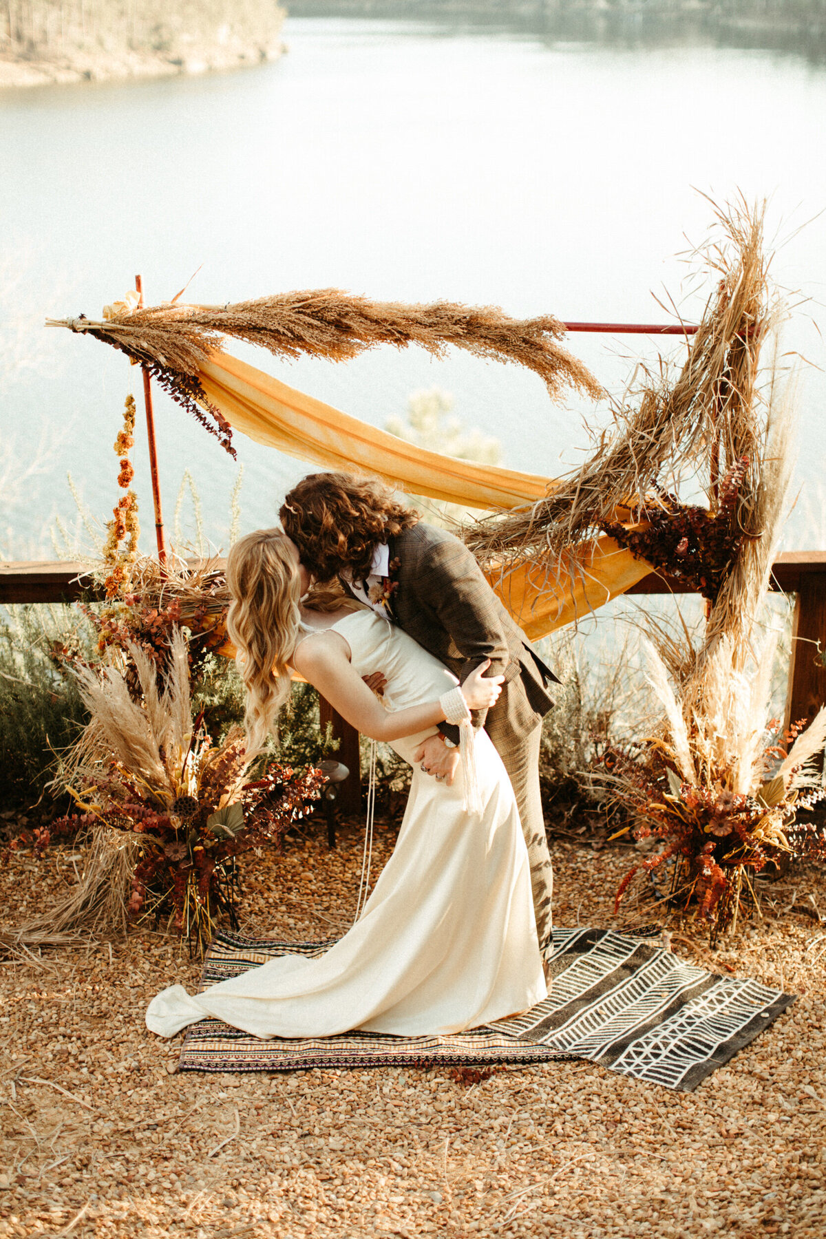 Boho bride and groom kissing during their intimate lakefront elopement ceremony