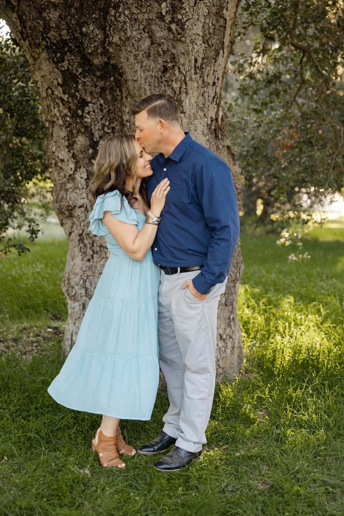 Mother and father standing close under a tree, sharing a sweet moment. Photographed by Yucaipa family photographer Kaitlyn Dawn Photography.