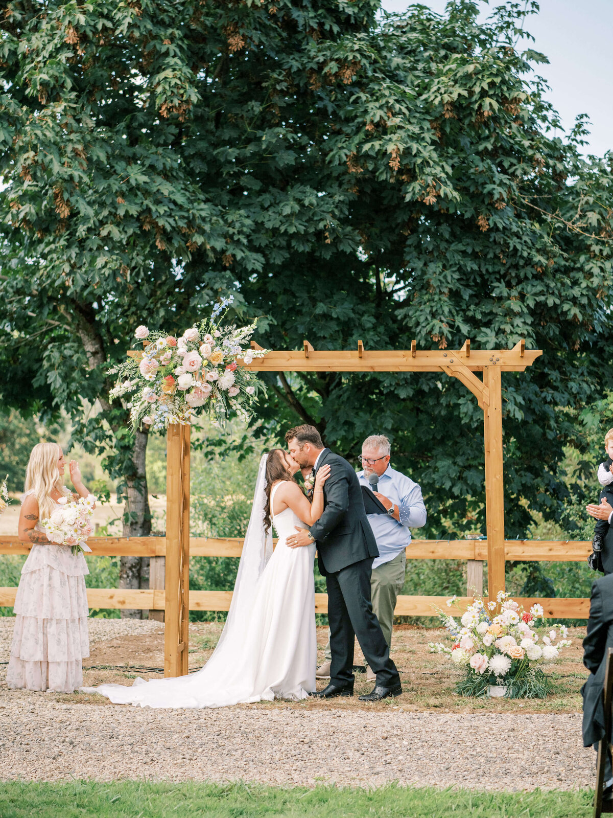A bride and groom kiss standing under a wooden arbor at their luxury backyard wedding in Oregon.