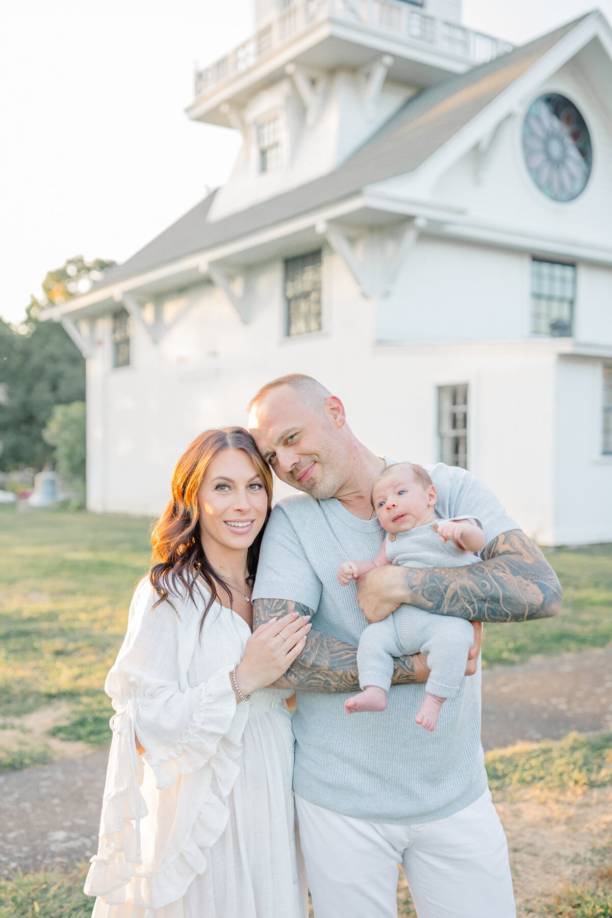 Family session in a beautiful evening outdoor location, where a husband and wife lovingly hold their newborn. The golden light of sunset enhances the warm, intimate moment as they embrace their new baby together
