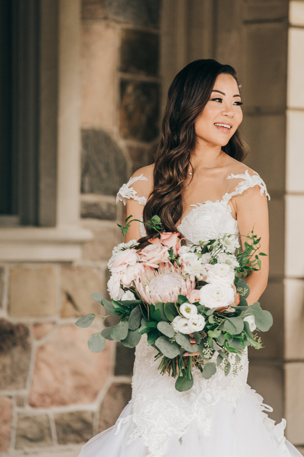 Beautiful bride smiling while holding bouquet of chrysanthemums and eucalyptus